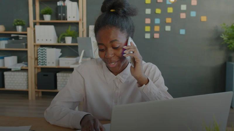 Young woman talking on phone at office desk with laptop
