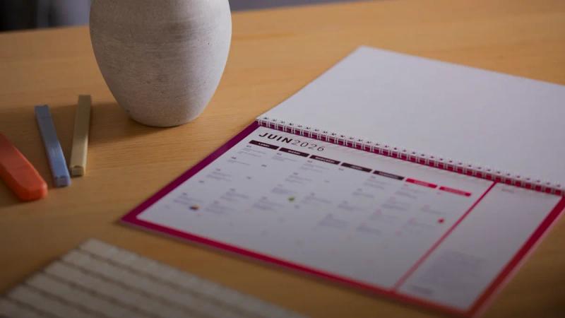 A calendar and vase sit on a wooden desk.