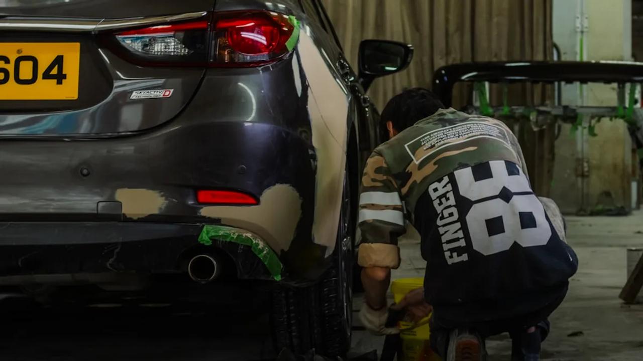 A person in a camouflage shirt repairing a car bumper in a workshop.