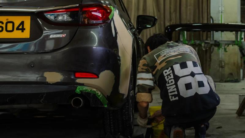 A person in a camouflage shirt repairing a car bumper in a workshop.