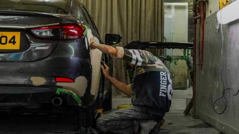 A person sanding the rear bumper of a grey car in a workshop