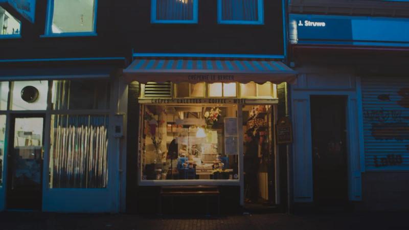 A brightly lit storefront illuminates a dark street at night