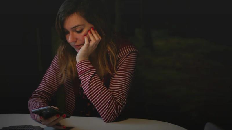 woman leaning on white wooden table while holding black Android smartphone