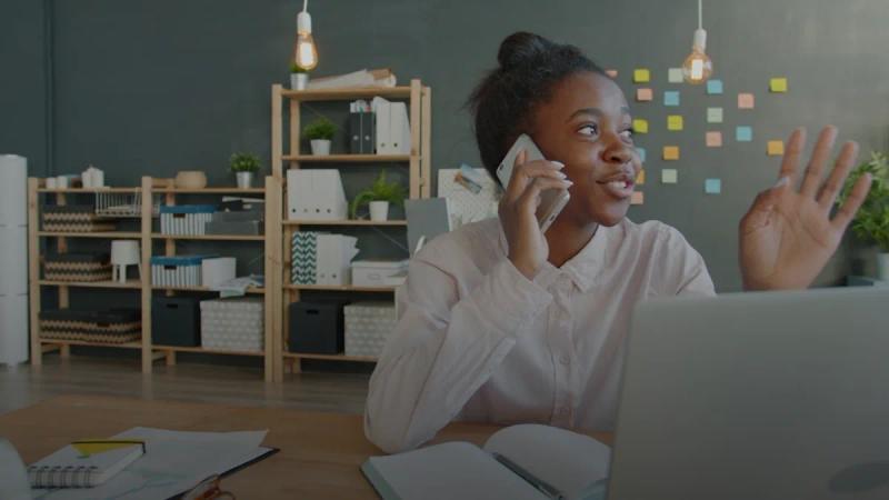 Young woman talking on phone at desk with laptop.