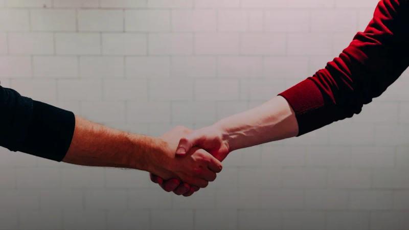 two person shaking hands near white painted wall