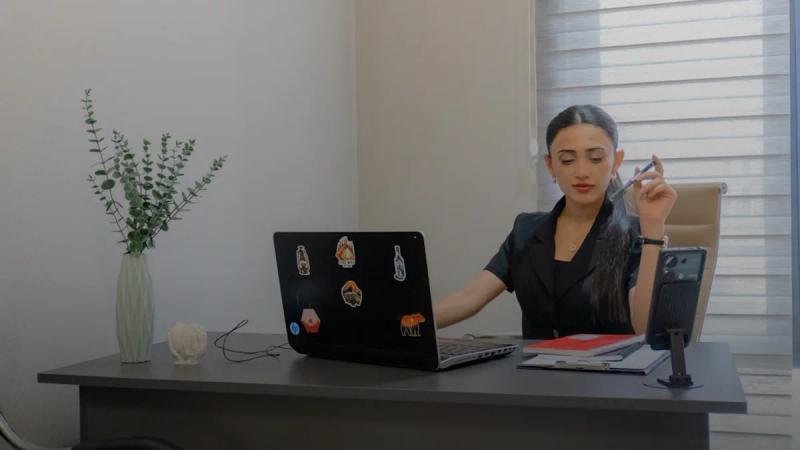 Woman working at desk with laptop and phone.