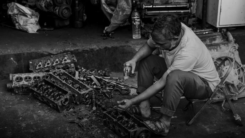 Man working on car engine parts outdoors.