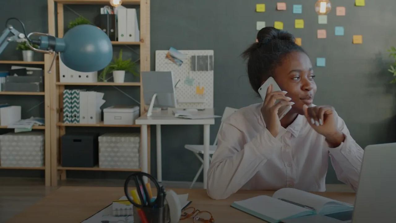 Woman talking on phone at desk in office.