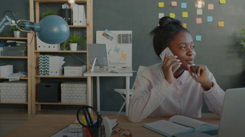 Woman talking on phone at desk in office.