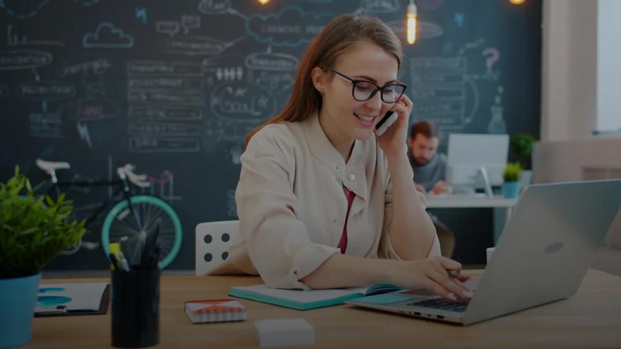 Woman talking on phone at desk with laptop