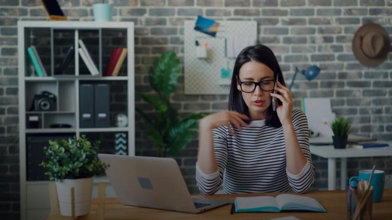 a woman sitting at a desk talking on a cell phone