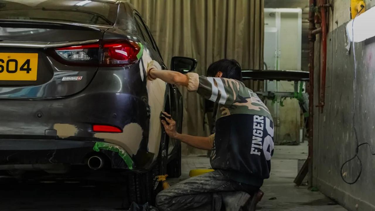 A person sanding the body of a grey car in an auto repair shop.