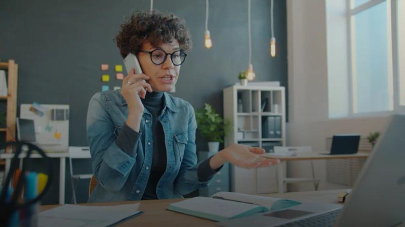 Woman talking on phone at desk with laptop.